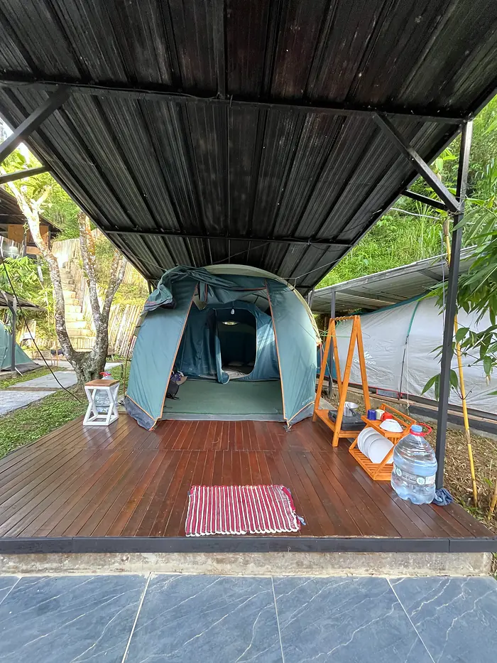 Tenda berdiri di atas deck kayu dengan lampu dan perlengkapan tamu
