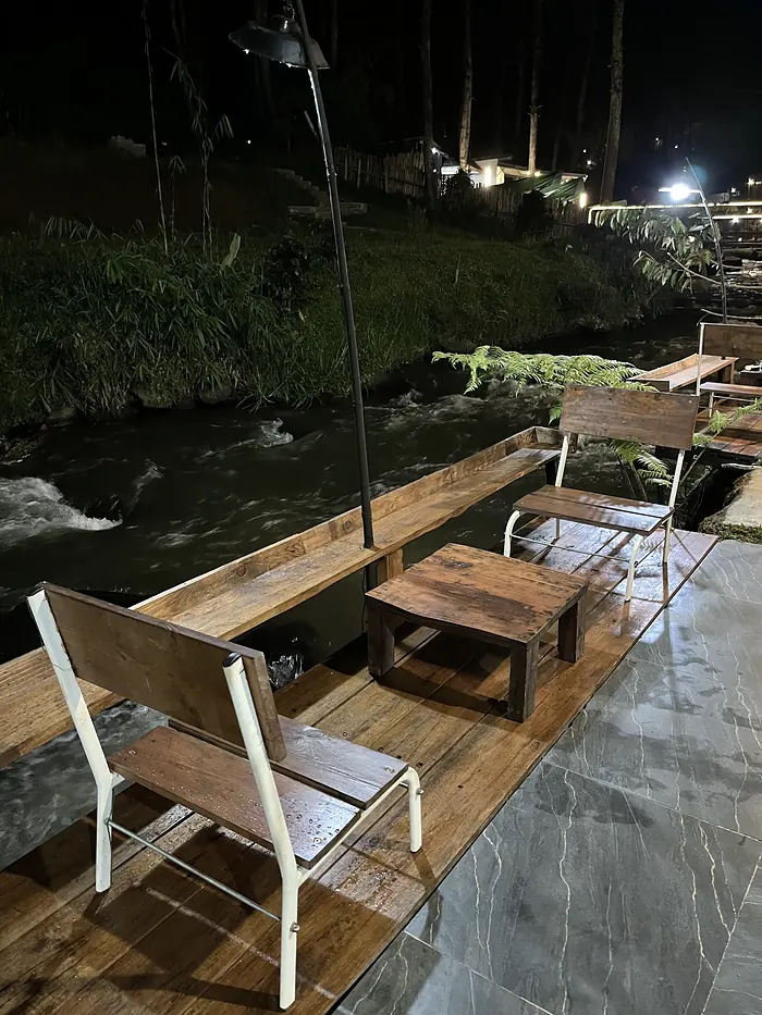 Kursi dan meja kayu di dek yang menghadap sungai pada malam hari