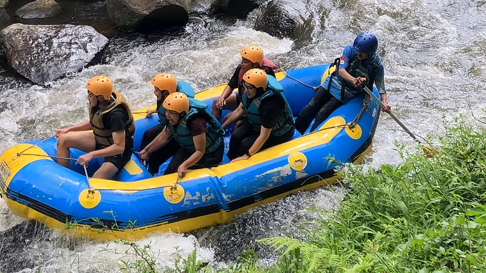 Perahu rafting berisi tamu melintasi bebatuan sungai